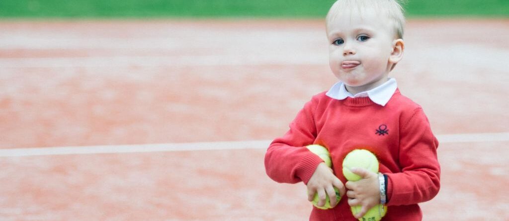 Tennis lastele: Punase kampsuniga poiss kunstmuru kattega tenniseväljakul